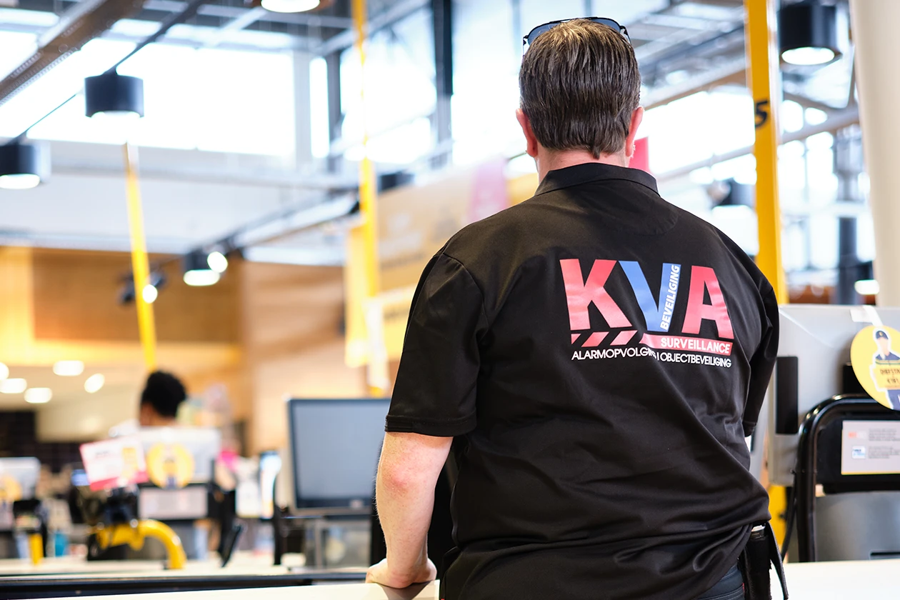 Medewerker van KVA Beveiliging staat in uniform bij de kassa van een supermarkt